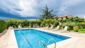Une piscine rectangulaire à l’eau d’un bleu limpide, entourée d’une terrasse en pierre et jouxtant un bâtiment dont le toit est recouvert de tuiles.