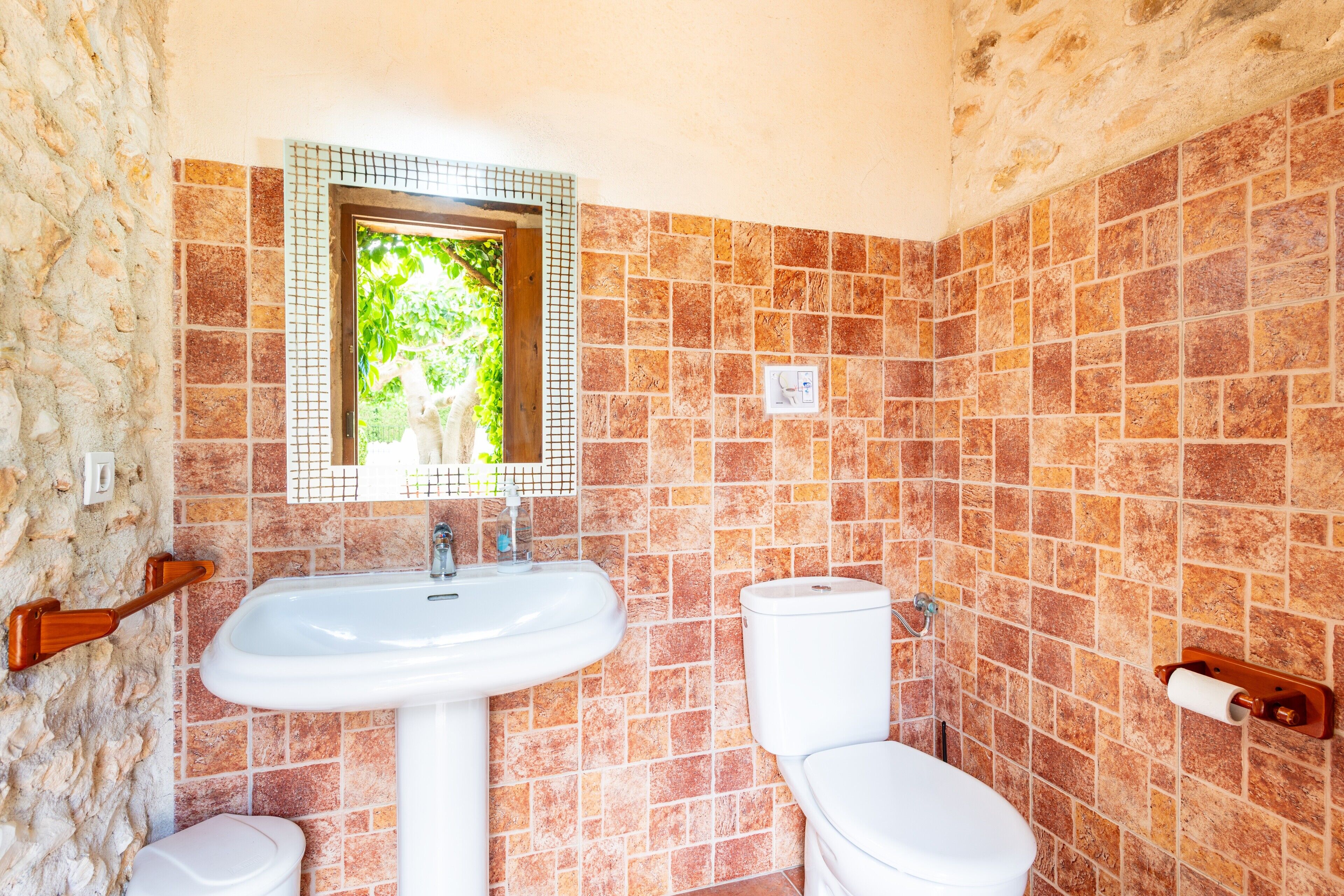 A bathroom with a sink, toilet, and a window with a view of greenery.