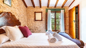 Une chambre avec un mur en pierre, des poutres en bois, un lit avec des oreillers, une fenêtre avec des rideaux et une porte en bois.
