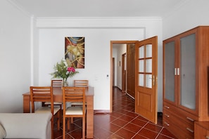 A dining area with a wooden table and chairs, a vase with flowers, and a painting on the wall.