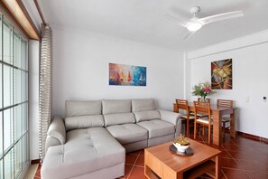A living room with a sectional sofa, dining table, chairs, ceiling fan, and two paintings on the wall.