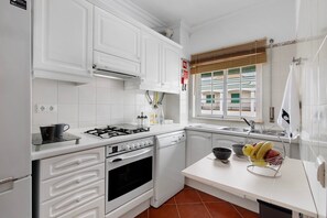A modern kitchen with white cabinetry, a gas stove, an oven, a dishwasher, and a window with blinds.