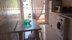 A compact kitchen with a washing machine, microwave, and a table with a bowl. - Apartment 'T1 Em Alvor' with Sea View, Shared Pool and Shared Garden (Alvor)
