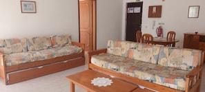 Una sala de estar con dos sofás, una mesa de centro de madera y una mesa de comedor con sillas.