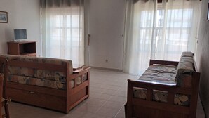 A living room with a sofa, a wooden table, and a television on a stand. - Apartment 'T1 Em Alvor' with Sea View, Shared Pool and Shared Garden (Alvor)