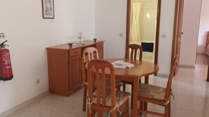 A dining area with a wooden table and chairs, a fire extinguisher, and a telephone on the wall. - Apartment 'T1 Em Alvor' with Sea View, Shared Pool and Shared Garden (Alvor)