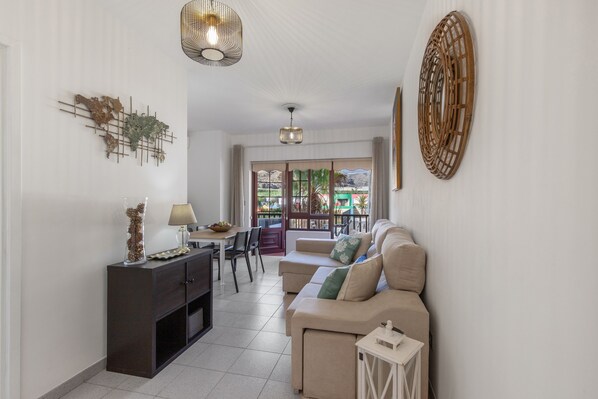 A living room with a sofa, a TV, a dining table, and a decorative wall piece.