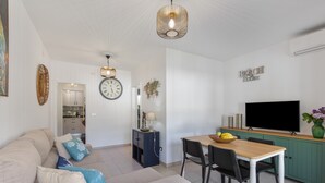 A modern living room with a sofa, dining table, chairs, a TV, and a kitchen area.