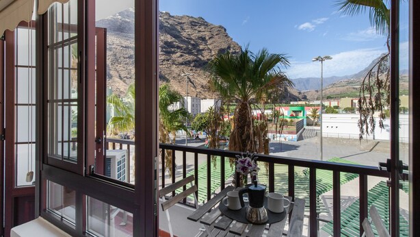 A balcony with a table, chairs, and a view of a mountain and buildings.