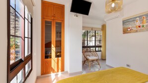 A room with a bed, a television, a wooden wardrobe, a chair, and a painting on the wall.