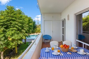 Un balcon avec une table à manger dressée pour le petit-déjeuner, offrant une vue sur une piscine et une végétation luxuriante.