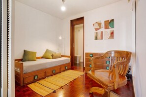 Een slaapkamer met een houten bed, een houten stoel, een klein houten dressoir en een geweven vloerkleed.