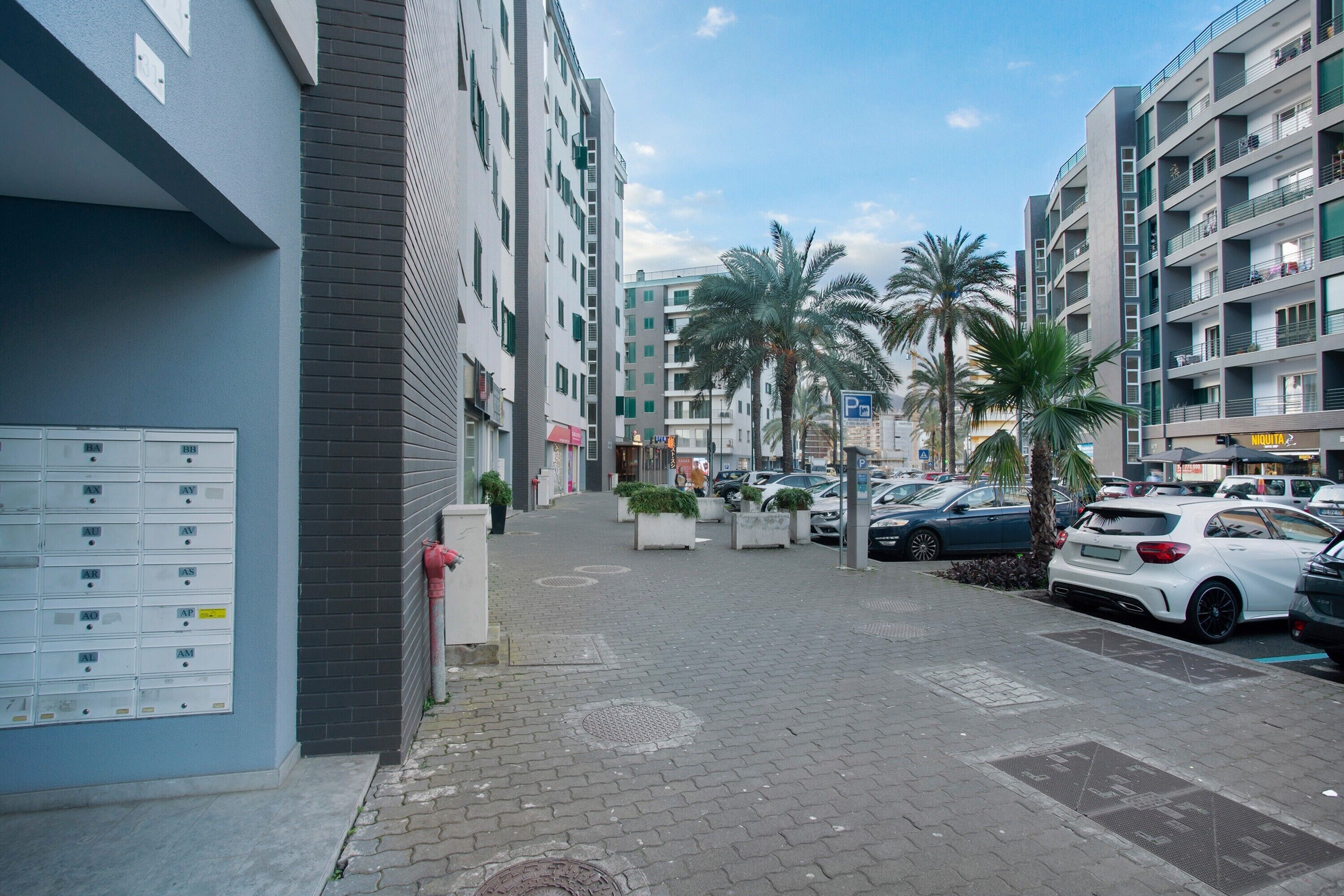 A multi-story building with a parking area, palm trees, and a clear sky.