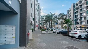 A multi-story building with a parking area, palm trees, and a clear sky.