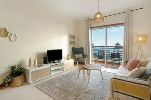 Una sala de estar moderna con un televisor de pantalla plana, un sillón verde, una mesa de centro redonda y un balcón con vistas.
