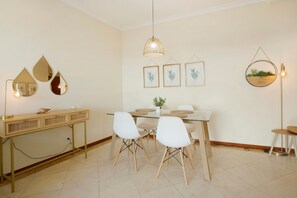 Un comedor con mesa de vidrio, sillas blancas, una consola dorada y decoración en la pared que incluye espejos e impresiones botánicas enmarcadas.