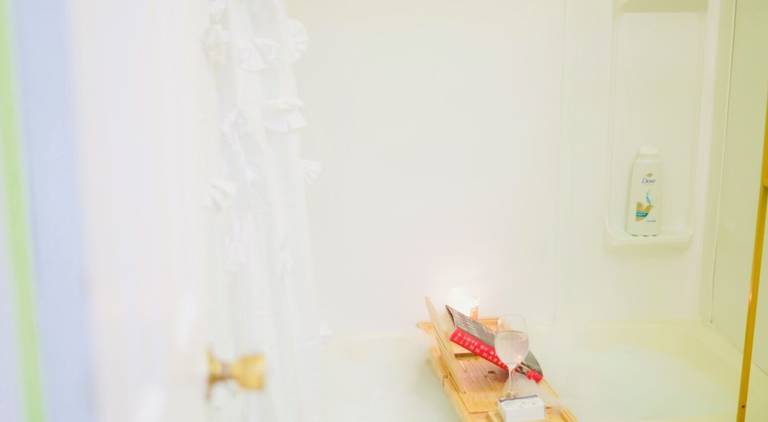 A bathroom with a white bathtub, a red toothbrush holder, and a bottle of Dove soap on the wall.