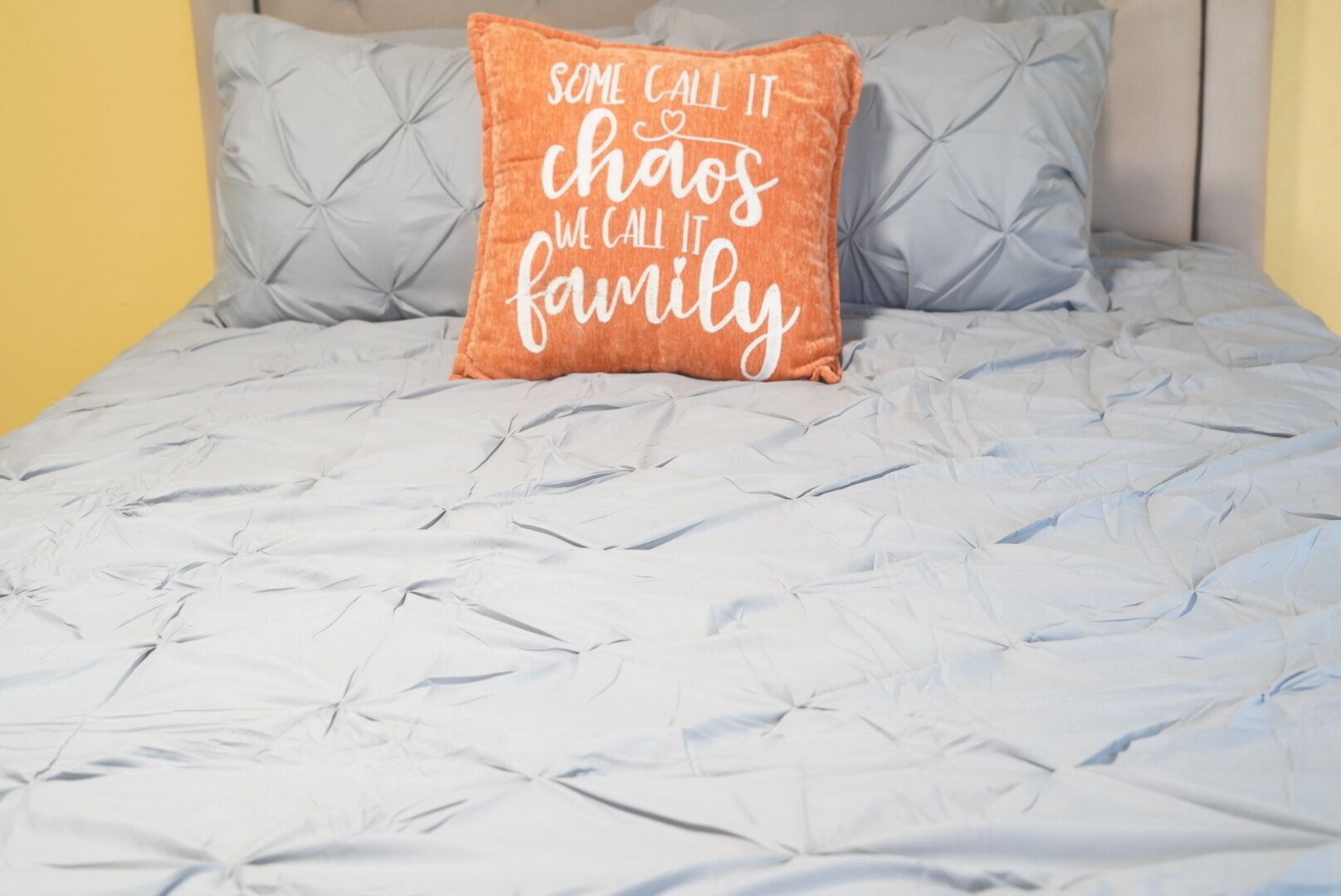 Una cama con edredón gris y almohada naranja con texto.
