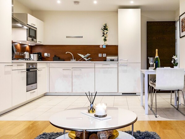 A modern kitchen with white cabinets, a built-in oven, and a dining area with a white table and chairs.