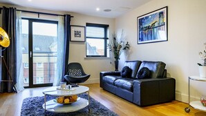 A modern living room with a black leather sofa, a round coffee table, and a large window with curtains. - City Centre | Cathedral Quarter | Walk Everywhere - Pass the Keys (Belfast)