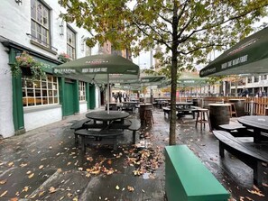 Een buitenzitplaats met tafels en parasols, omringd door gebouwen.