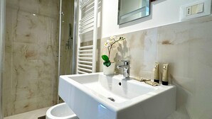 A modern bathroom with a white sink, a glass shower enclosure, and a potted orchid.