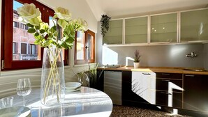 A modern kitchen with a round dining table, a vase with flowers, and a view of the street outside.