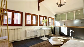 A hotel room with a dining table, chairs, a radiator, a chandelier, and a view of the outside through large windows. - Surian Loft (200m from St Mark’s Square) (Venecia)