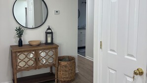 A hallway with a wooden console table, a round mirror, a small plant, a lantern, and a white door.
