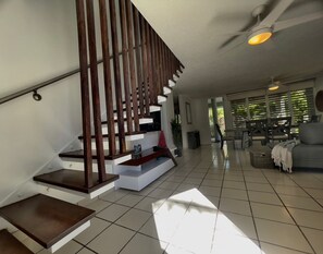 Uma área de estar ampla com uma escada moderna, um sofá e um ventilador de teto.