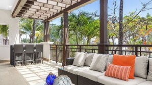 A covered outdoor seating area with a sofa, cushions, and a table with decorative items. - Renovated 2-bedroom condo with WiFi, AC inside Bahía Beach Resort (Río Grande)