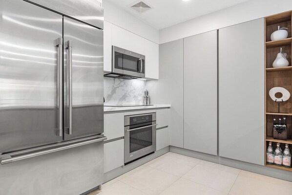 A modern kitchen with stainless steel appliances, a microwave, oven, and a built-in wine rack with bottles. - Renovated 2-bedroom condo with WiFi, AC inside Bahía Beach Resort (Río Grande)