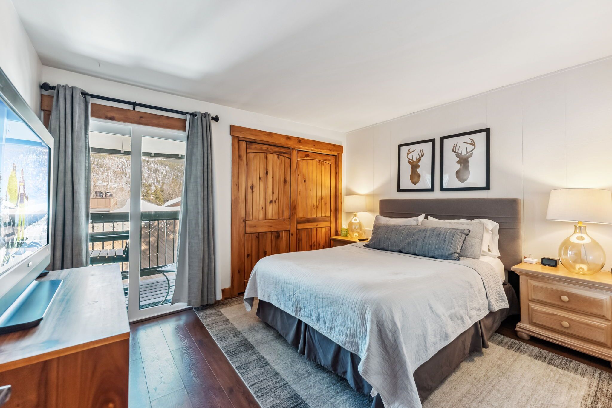 A bedroom with a large bed, wooden wardrobe, and a TV on a wooden desk.