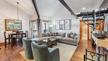 A spacious living room with a wooden dining table, grey sofas, and a staircase with a cat tree.