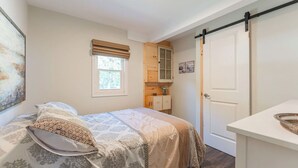 A bedroom with a bed, a window with blinds, a wooden cabinet, and a door.