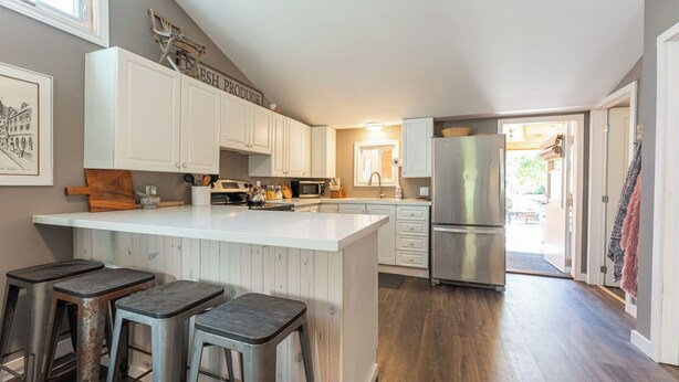 A modern kitchen with white cabinetry, a central island with stools, stainless steel appliances, and a view to the outdoor area.