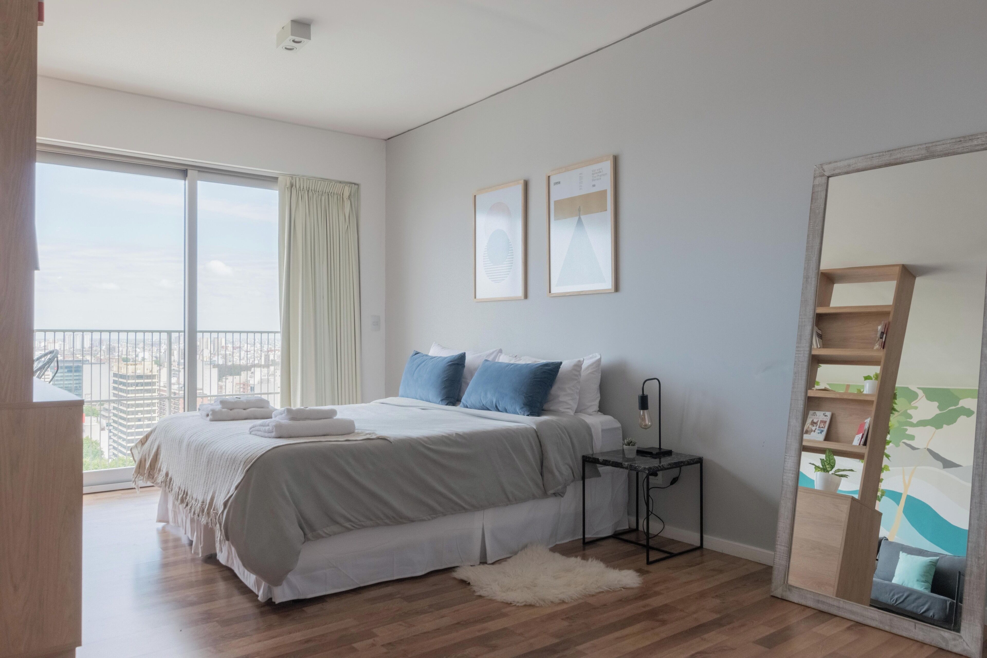 Une chambre à coucher avec un grand lit, une table de chevet, un miroir et une vue sur l’extérieur.