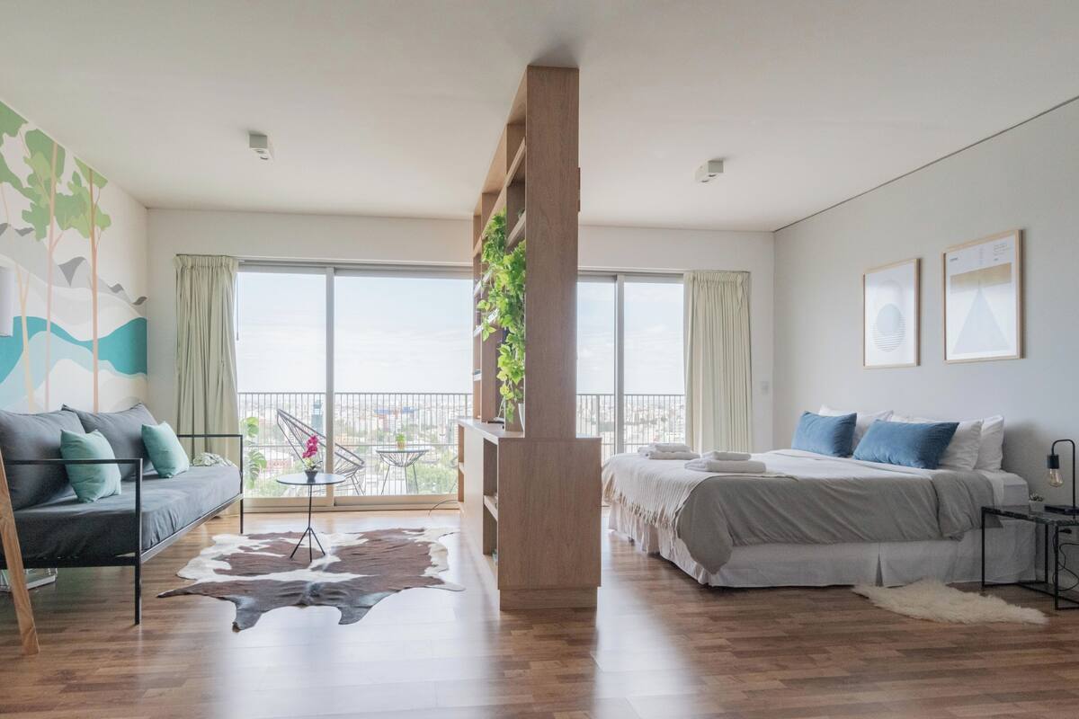 A modern bedroom with a large bed, a sofa, and a balcony with a view.