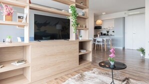 A modern living room with a large flat-screen TV, wooden shelving with decorative items, a round coffee table, and a fur rug. - MOT Azopardo 700 (Buenos Aires)