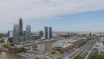 Un paysage urbain avec des immeubles modernes de grande hauteur, une rivière et une rue animée où circulent de nombreux véhicules.