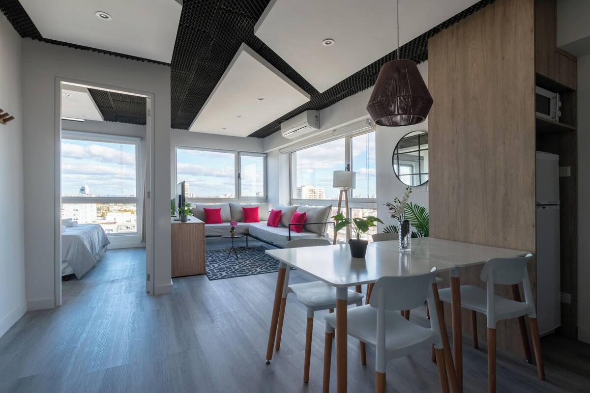A modern living room with a dining area, large windows, and a city view.