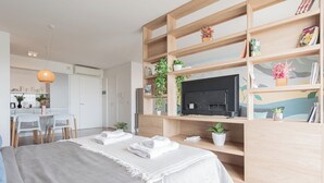 A modern bedroom with a large bed, a TV, a wooden bookshelf, and a dining area. - MOT Azopardo 700 (Buenos Aires)