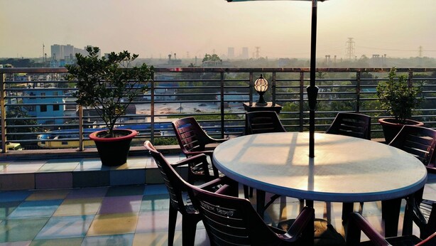 Una terraza con una mesa redonda y sillas, una sombrilla grande y plantas en macetas.