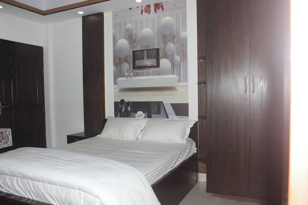 A bedroom with a bed, a TV mounted on the wall, and a wardrobe.