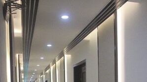 Un pasillo largo y bien iluminado con puertas a un lado y un suelo reflectante.