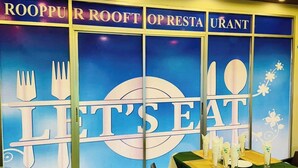 Un interior de restaurante con un letrero que dice 'Let's Eat', una mesa cubierta con mantel verde y sillas.