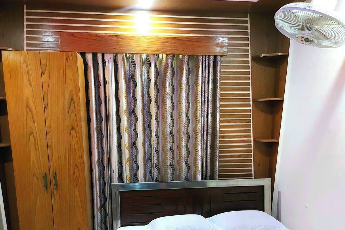 A bedroom with a bed, wooden wardrobe, and a ceiling light fixture.