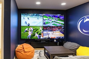 Un grand mur d’écrans diffusant différentes compétitions sportives, un logo sur le mur et un espace détente avec des fauteuils-pouf et des coussins.