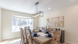 Un coin repas avec une table et des chaises en bois, un luminaire suspendu et une fenêtre donnant sur les arbres.