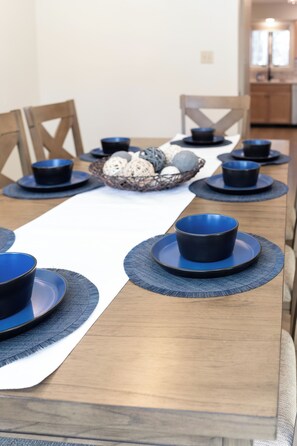 Een eettafel gedekt met blauwe kommen en borden, een geweven tafelonderzetter, en een mand met decoratieve objecten.